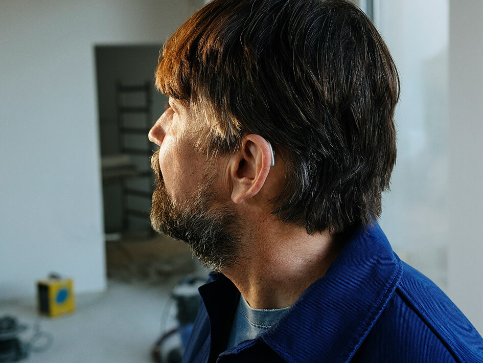 Mann mit Bart, Hörgerät und blauer Jacke.