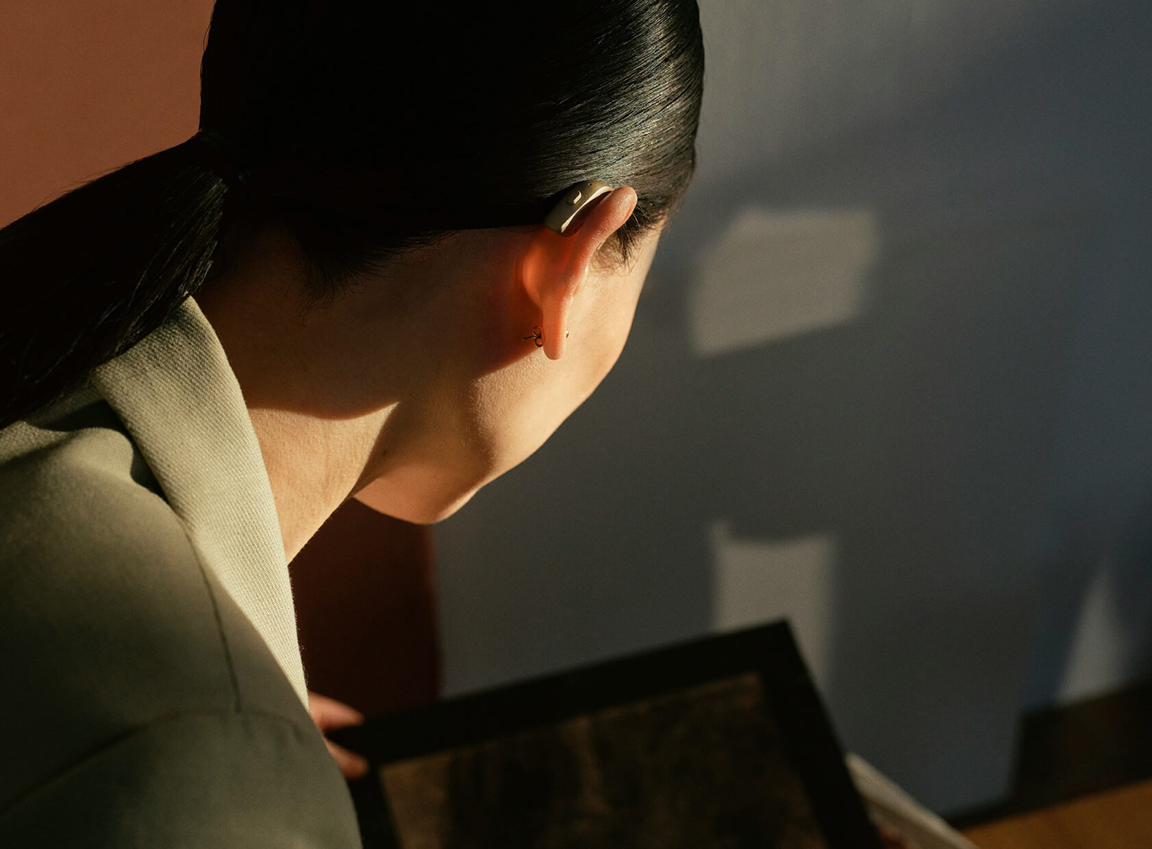 Person von hinten mit Gerät am Ohr blickt auf Gegenstand.