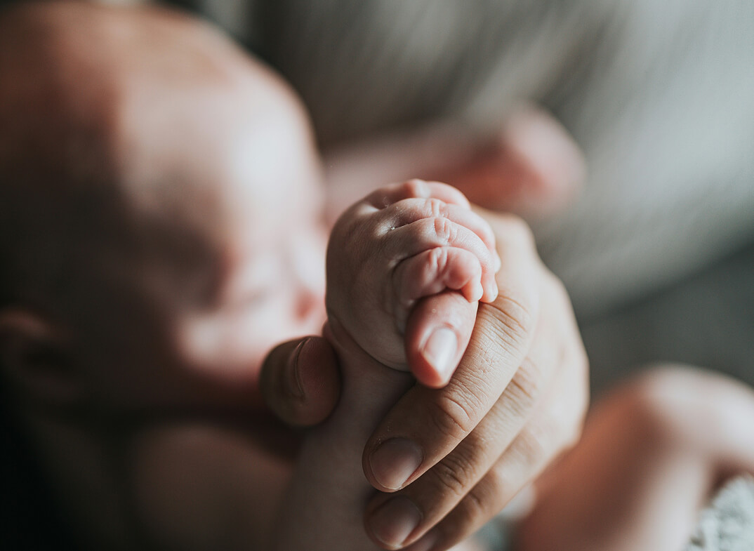 Nahaufnahme: Babyhand umschließt Erwachsenenfinger.