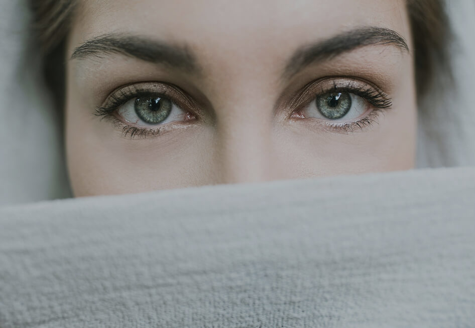 Zwei Augen blicken über hellen Stoff hervor.