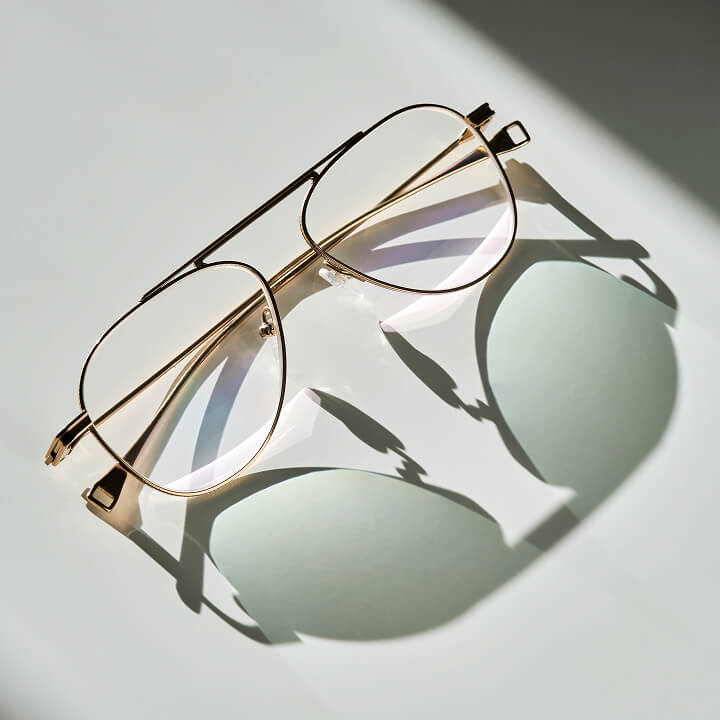 Goldene Aviator-Brille auf hellem Grund mit Schatten.
