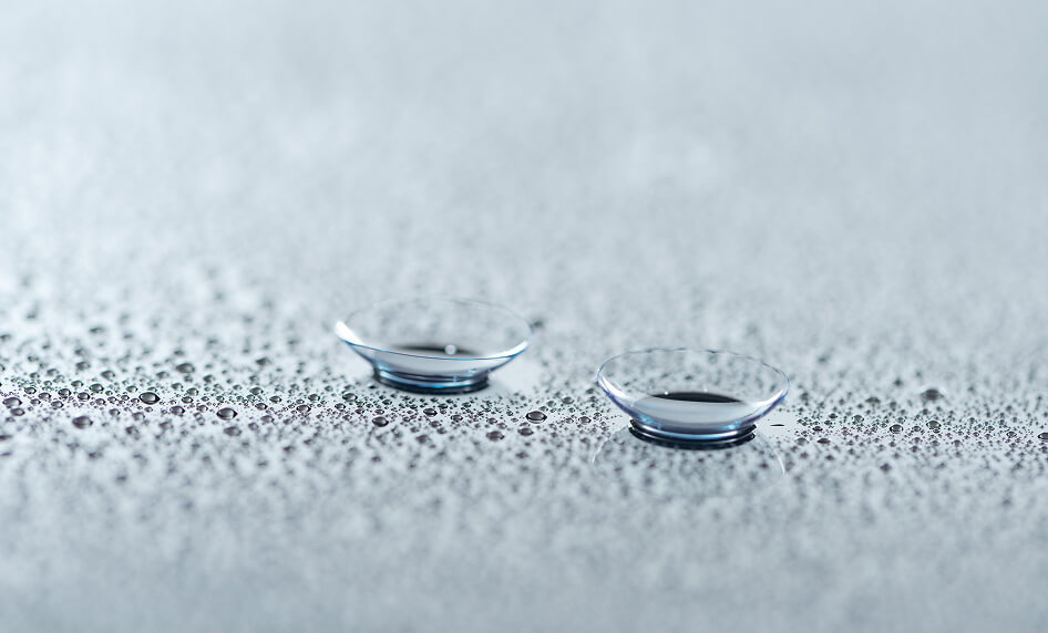 Zwei Kontaktlinsen auf einer Oberfläche mit Wassertropfen.
