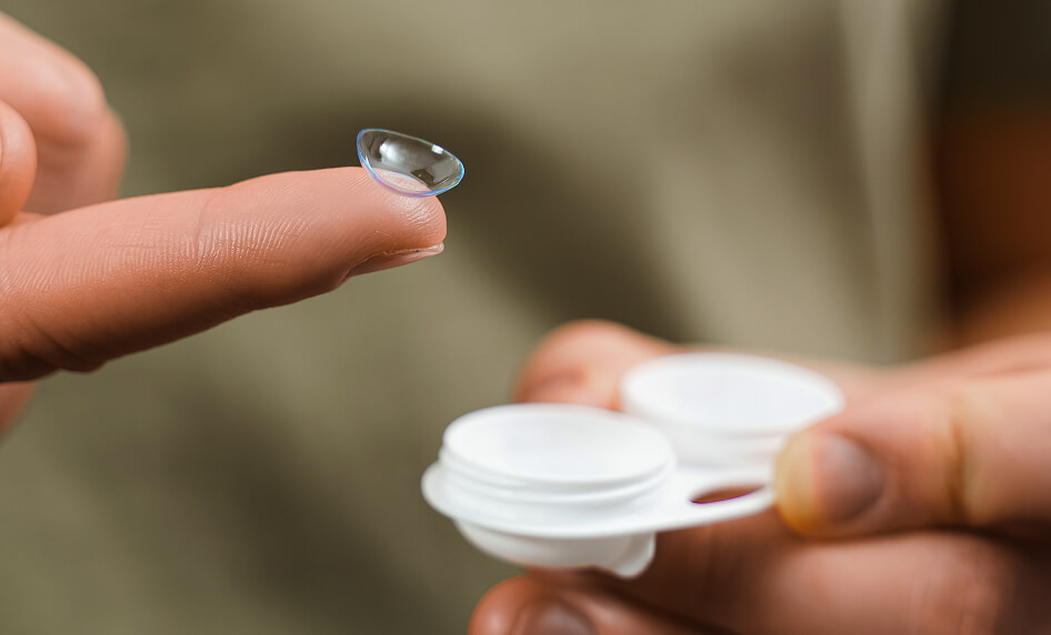 Finger hält Kontaktlinse über Behälter.