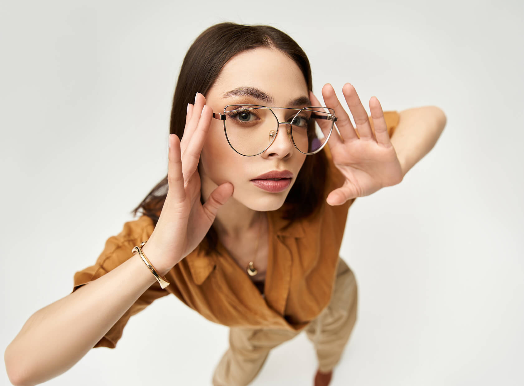 Frau mit Brille blickt zur Kamera, Hände erhoben.