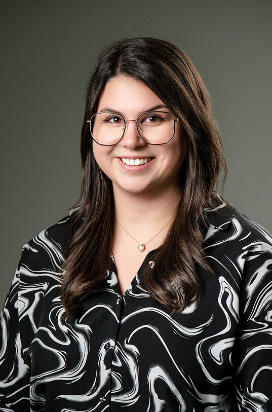 Lächelnde Frau mit Brille und gemusterter Bluse.