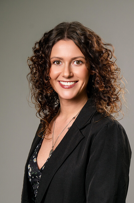 Lächelnde Frau mit lockigem Haar und schwarzem Blazer.