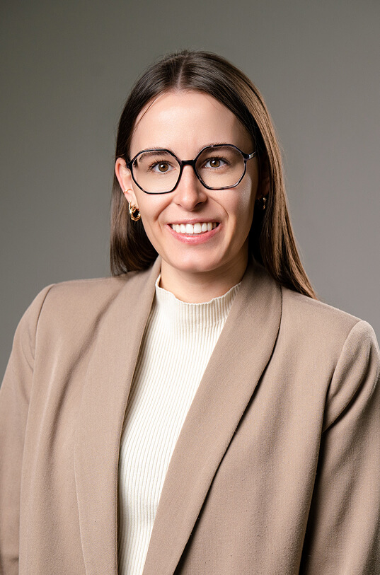 Lächelnde Frau mit Brille, Blazer und cremefarbenem Pullover.