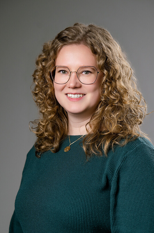 Lachende Frau mit lockigem Haar, Brille und grünem Oberteil.