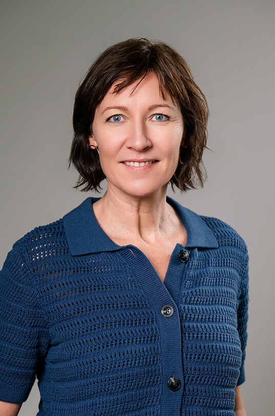 Lachende Frau mit blauen Augen und blauer Strickjacke.