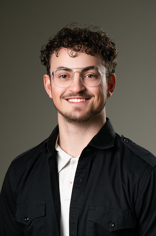Junger Mann mit Locken, Brille, Bart, lächelt.