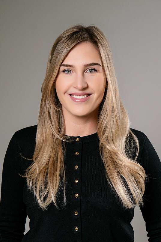 Blonde Frau in schwarzer Strickjacke lächelt.