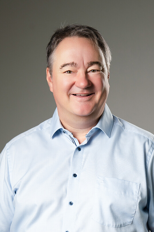 Mann lächelt, trägt hellblaues Hemd.